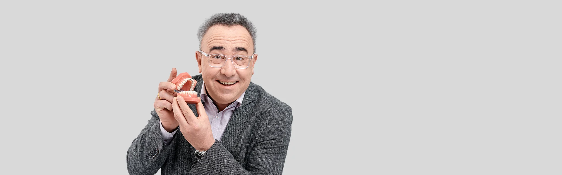 Lächelnder Mann mit Brille zeigt Kiefermodell mit Zahnspange