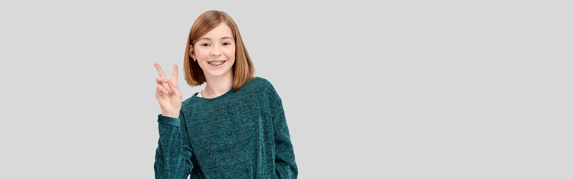 Mädchen mit Zahnspange zeigt lachend das Peace-Zeichen
