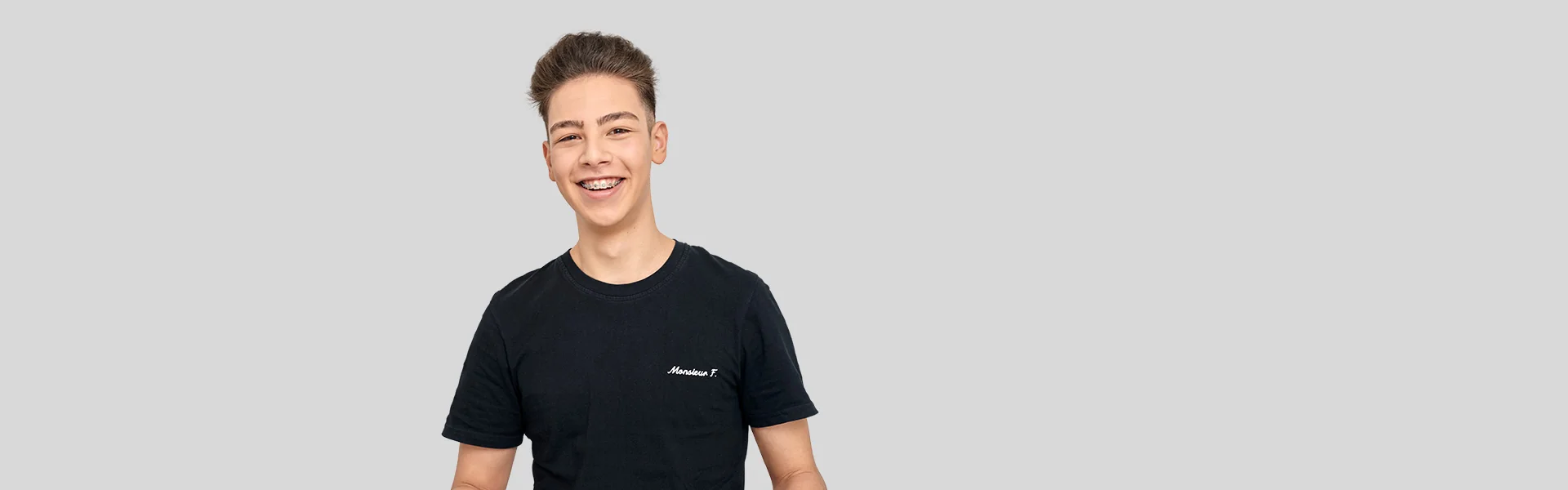 Lachender Teenager mit Zahnspange im schwarzen T-Shirt