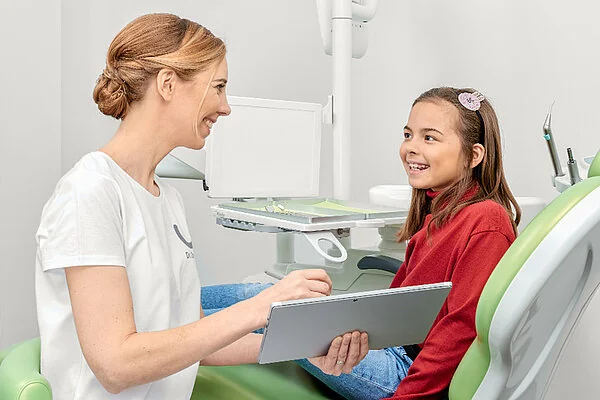 Behandlerin mit Tablet im Gespräch mit einer jungen Patientin auf dem Behandlungsstuhl
