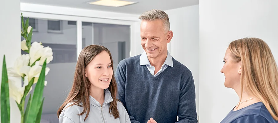 Lachende Familie in der Praxis: Tochter mit Zahnspange, Vater und Mutter